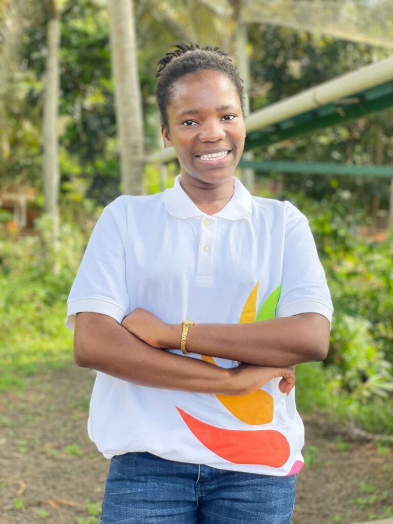 A young lady in a white top. She is smiling and her hands are crossed on her chest.