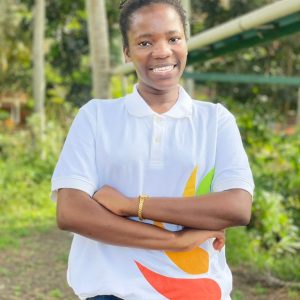 A young lady in a white top. She is smiling and her hands are crossed on her chest.